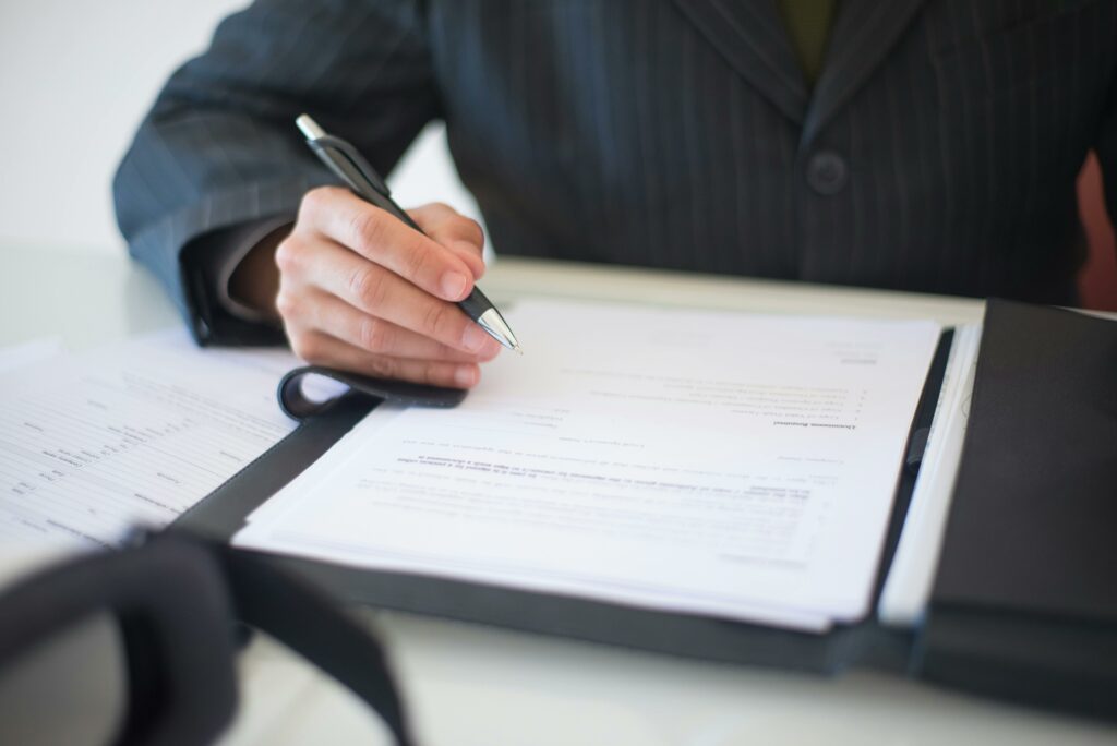 le buste d'un homme en costume assis sur son bureau. Il tient un stylo en main en train de lire des papiers administratifs. nos prestations de services proposent des aides administratives pour les personnes ayant des difficultés à faire les procédures par elles-mêmes.
