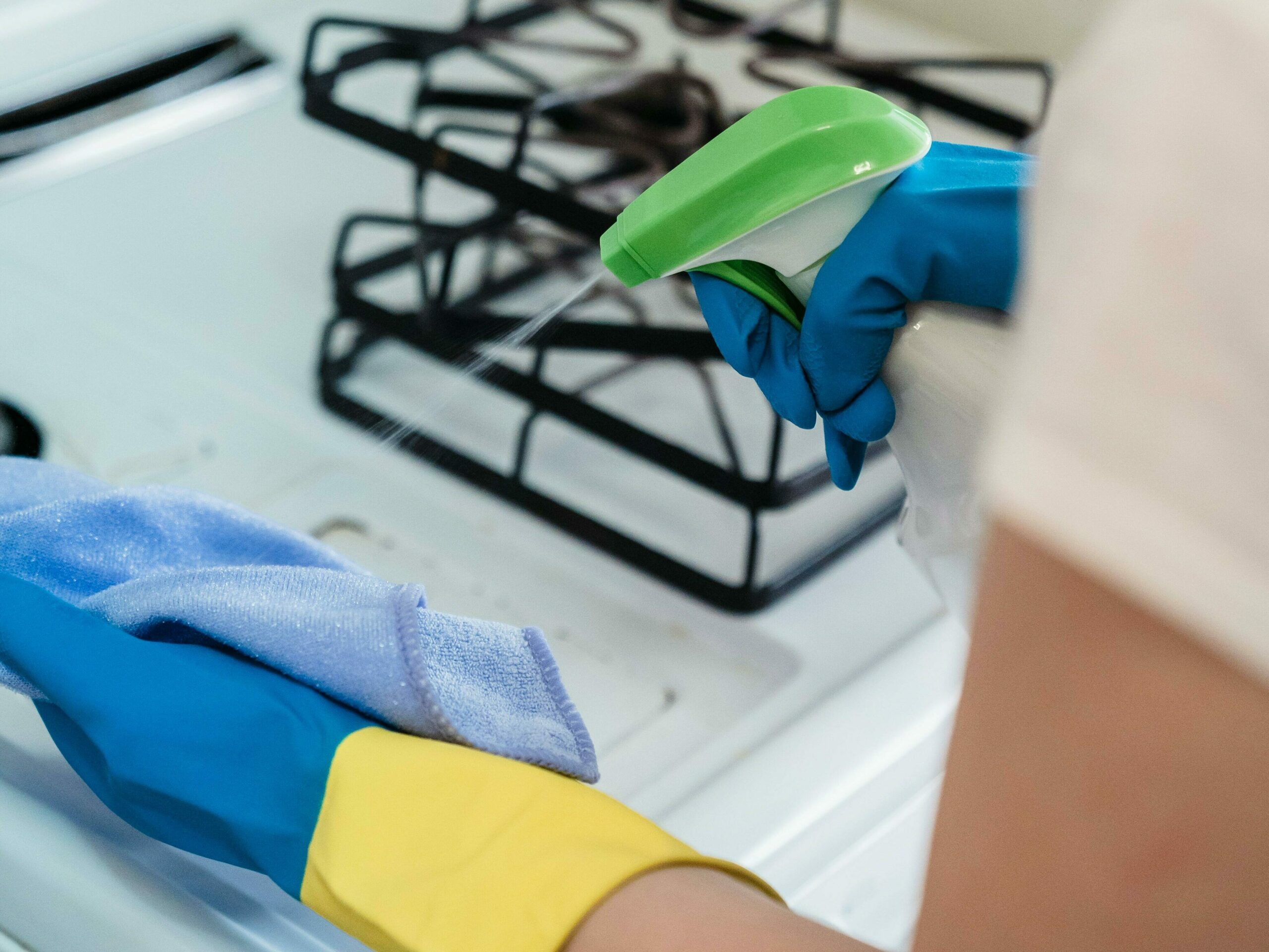 cette image représente les bras d'une personne au dessus d'une cuisinière. Un chiffon dans la main gauche, un produit ménager dans la main droite, cette personne s'apprête à nettoyer la cuisinière. nos services d'aide à domicile antibes permettent ce nettoyage impeccable