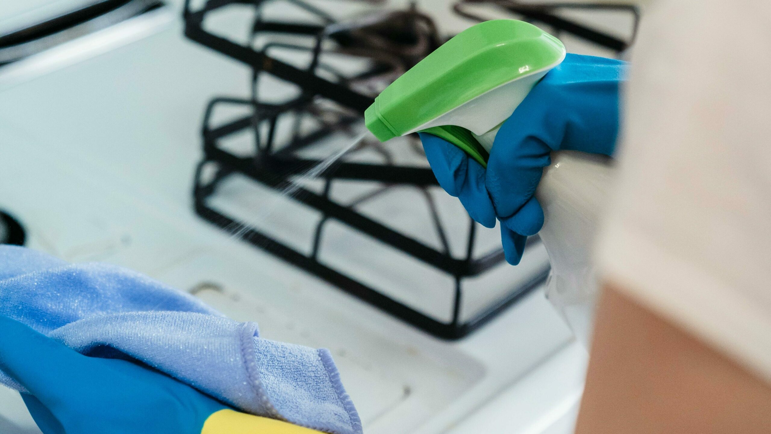 cette image représente les bras d'une personne au dessus d'une cuisinière. Un chiffon dans la main gauche, un produit ménager dans la main droite, cette personne s'apprête à nettoyer la cuisinière. nos prestations de services permettent ce nettoyage impeccable