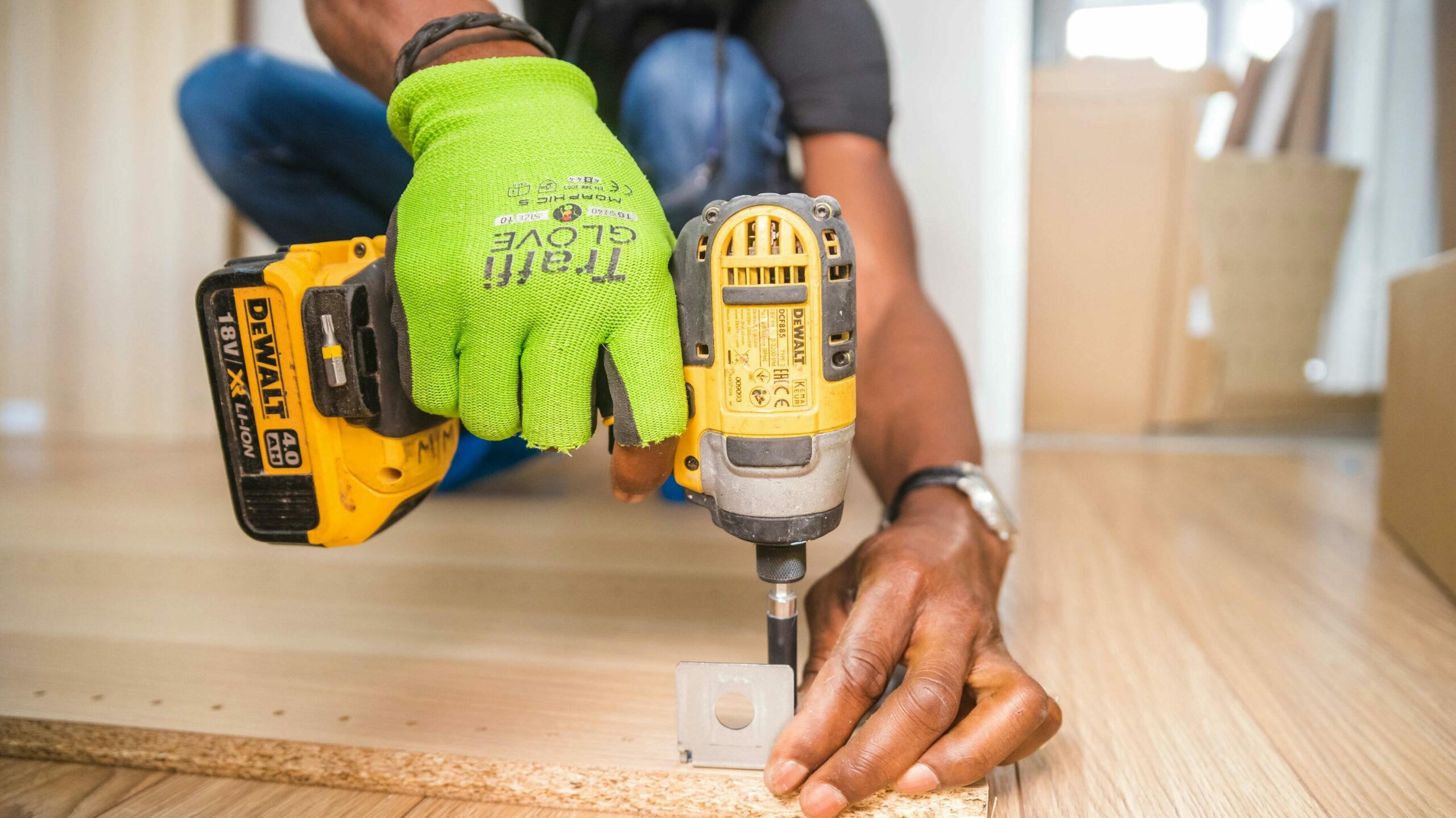 Un homme ganté qui tient une perceuse et perce un joint en métal dans une planche en bois. nos prestations de services proposent tous types de travaux et jardinages.