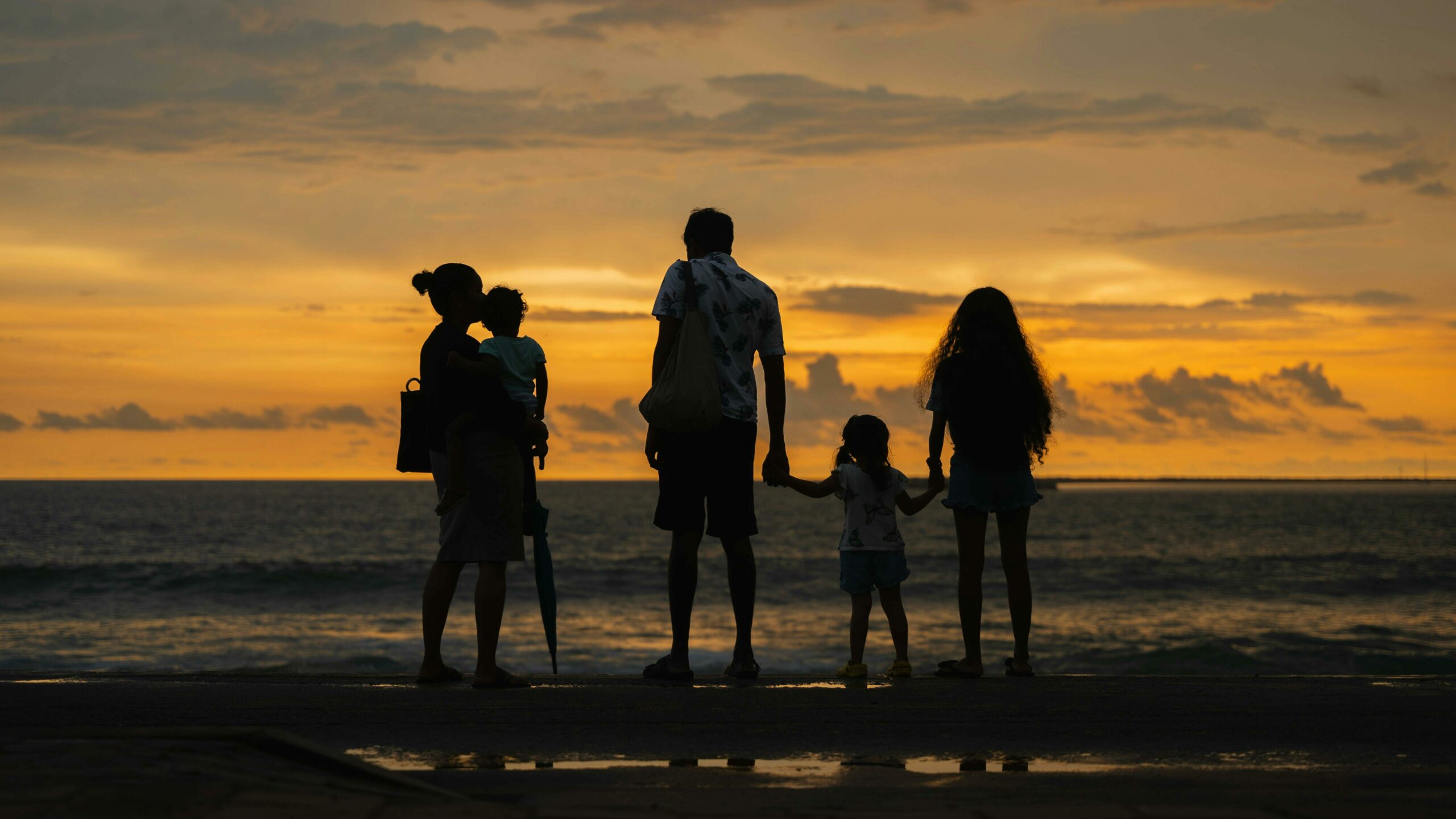 Silhouette d'une famille unie face à la mer au coucher du soleil, illustrant l'importance de l'entourage pour repérer les premiers signes d'isolement chez une personne âgée.